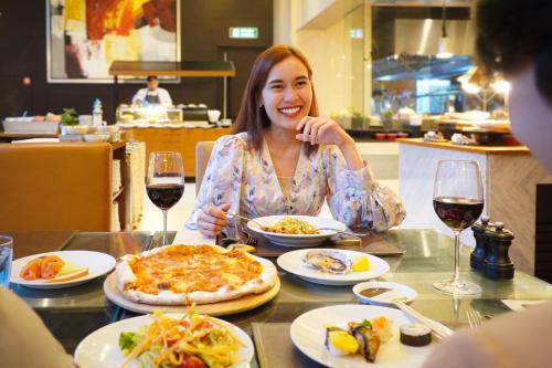 a woman sitting at a table with a pizza at Marriott Executive Apartments Sukhumvit Park, Bangkok in Bangkok
