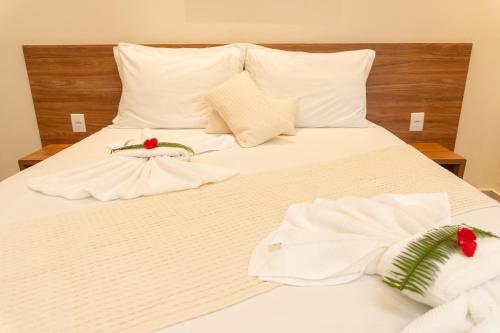 a white bed with white sheets and red flowers on it at Vila da Mata Chalés in Alto Paraíso de Goiás