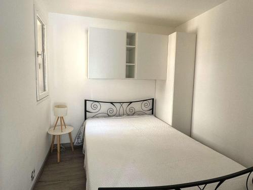 - une petite chambre blanche avec un lit et une table dans l'établissement Charmant T2 Climatisé avec Parking Privé, Jardinet, à 900m de la Plage Roquille - FR-1-607-202, au Cap d'Agde