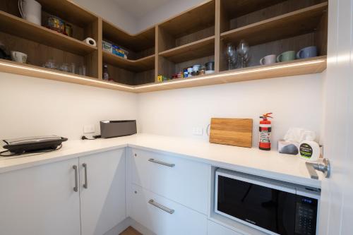 a kitchen with white cabinets and a microwave at Doubtless Delight - Cable Bay Holiday Home in Cable Bay