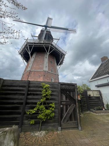 a building with a windmill behind a wooden fence at B&B Het Molenhuisje Winschoten - met woonkamer & keuken in Winschoten