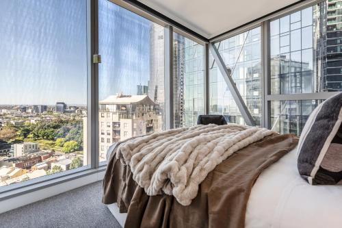 a bedroom with large windows and a bed with a blanket at West Side Explore Downtown Melb in Chic Condo in Melbourne