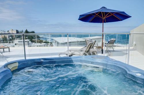 a hot tub on a balcony with an umbrella at Hamptons Style Penthouse at Kings Beach in Caloundra