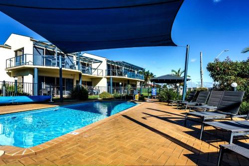 a swimming pool with chairs and a building at Sails 5 in Merimbula