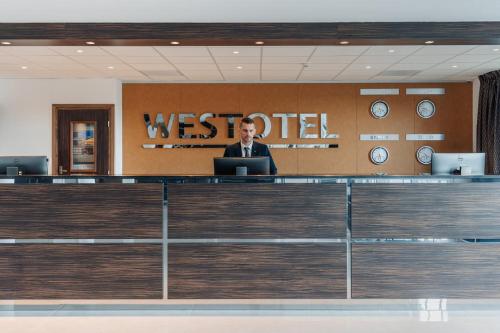 a man in a suit sitting at a desk in a lobby at Westotel Taverny - Paris Val-d'Oise in Taverny