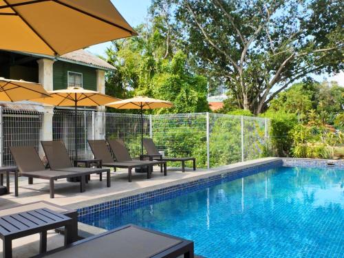 a swimming pool with chairs and umbrellas next to a swimming pool at Rucksack Inn Premium Melaka in Melaka