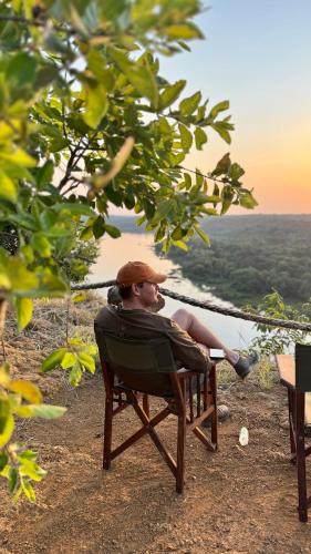 a man sitting in a chair looking out at the ocean at Hemingway's Luxury Tented Camp in Paraa