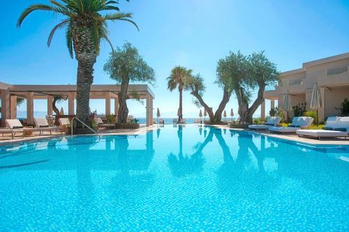 a swimming pool with palm trees and a hotel at Domes Miramare, a Luxury Collection Resort, Corfu - Adults Only in Moraitika
