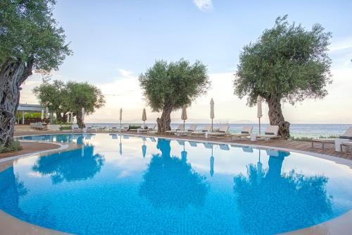 a swimming pool with trees and umbrellas and the ocean at Domes Miramare, a Luxury Collection Resort, Corfu - Adults Only in Moraitika