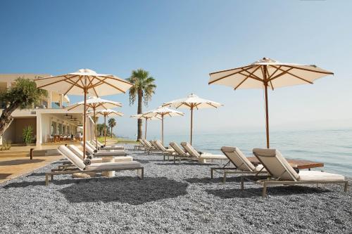 a row of lounge chairs and umbrellas on a beach at Domes Miramare, a Luxury Collection Resort, Corfu - Adults Only in Moraitika