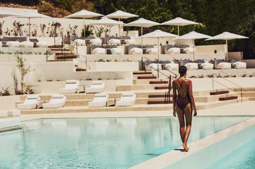 a woman in a swimsuit standing on the edge of a swimming pool at Domes Miramare, a Luxury Collection Resort, Corfu - Adults Only in Moraitika