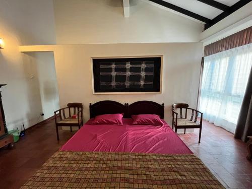 AttidiyaにあるSerene Villa with Pool & Large Gardenのベッドルーム1室(ピンクのシーツと椅子2脚付きのベッド1台付)