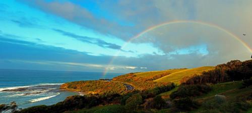 a rainbow in the sky over the ocean and a road at Points South By The Sea in Apollo Bay