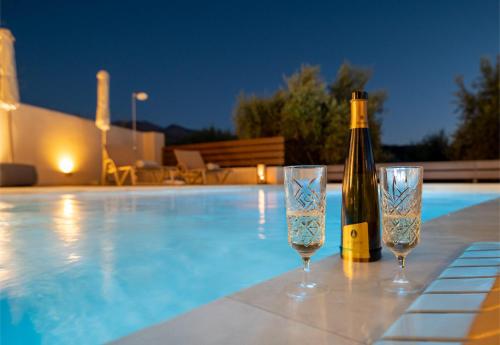 a bottle of wine and two glasses next to a swimming pool at Pavlina Villa , a hidden gem with heated pool and ping pong! in Perama