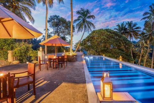 a pool at a resort with tables and umbrellas at Athulya Villas, Kandy in Kadugannawa