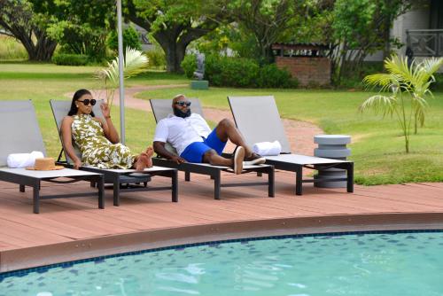 a man and woman sitting in lawn chairs next to a pool at Cresta Lodge Harare in Harare