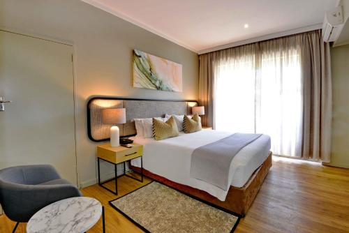 a bedroom with a bed and a chair and a window at Cresta Lodge Harare in Harare