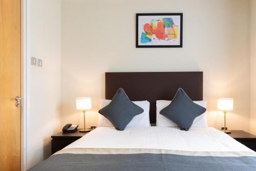 a bedroom with a bed with blue pillows and two lamps at Grand Plaza Serviced Apartments in London