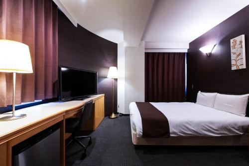 a hotel room with a bed and a desk with a television at Urvest Hotel Kamata in Tokyo