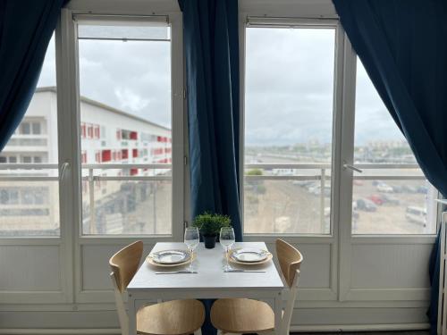 une table blanche avec deux chaises et deux fenêtres dans l'établissement La Mouette, à Calais