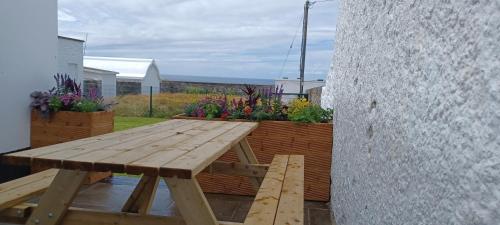 a wooden picnic table on a patio with flowers at Loop Head Lighthouse Attendant's Cottage in Kilbaha