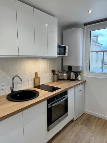 une cuisine avec des armoires blanches, un évier et une fenêtre dans l'établissement Le Cheval Gris - Cathédrale - Hyper Centre, à Chartres