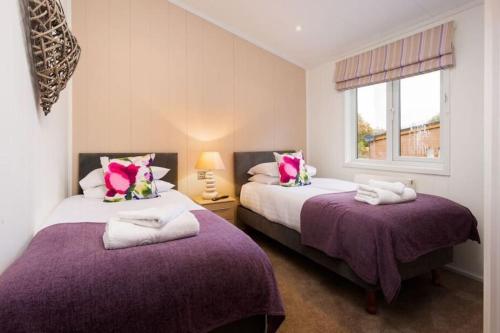 two beds in a room with purple sheets and a window at Driftwood Lodge - South Lakeland Leisure Village in Carnforth