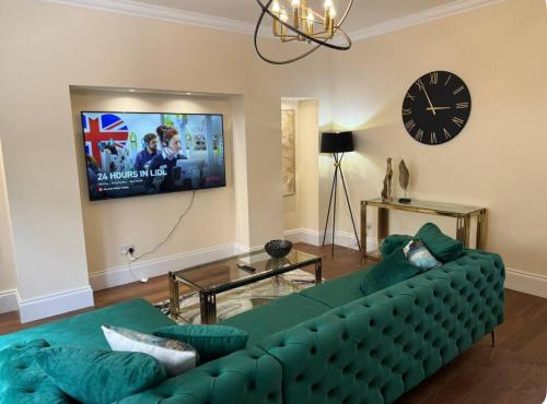 a living room with a green couch and a clock at Glasgow Central Paradise - Spacious 3- Bed House in Glasgow