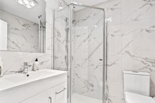 a white bathroom with a shower and a sink at Ventura Delight Townhouse with Parking and Patio in Auckland