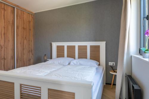 a bedroom with a white bed with a wooden headboard at Luxe 4 pers chalet op minicamping in waarde in Waarde