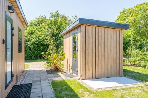 a wooden shed with a door next to a house at Luxe 4 pers chalet op minicamping in waarde in Waarde
