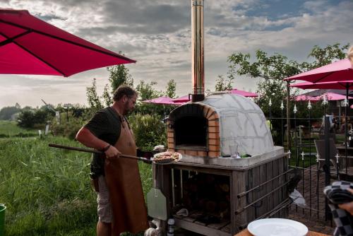 a man is cooking food in an outdoor oven at Luxe 4 pers chalet op minicamping in waarde in Waarde