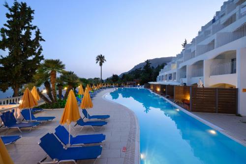 a swimming pool with chairs and umbrellas next to a hotel at Sunshine Corfu Hotel And Spa in Nisakion