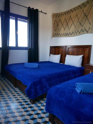 two beds in a room with blue sheets and a window at Dar Iziki in Sidi Kaouki