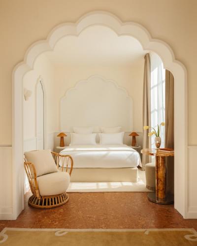 a white bedroom with a bed and a chair at LILOU in Hyères