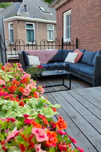 a patio with a blue couch and flowers on a deck at Om De Hoek in Norg