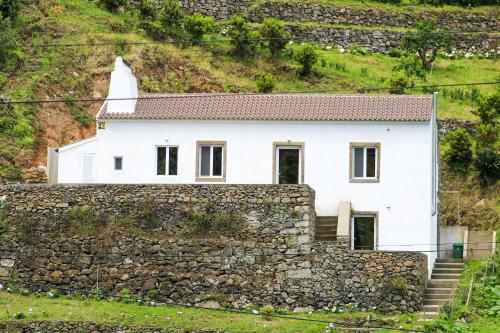a white house on top of a stone wall at Casa da Eira in Faial da Terra