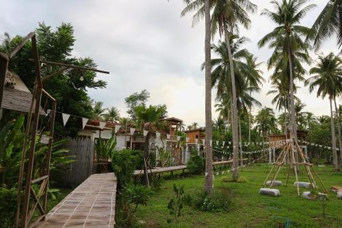 a wooden path leading to a resort with palm trees at บ้านพราวพร้าว Baan Proud Proud in Khanom