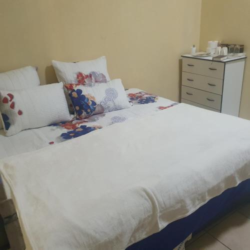 a white bed with pillows and a dresser in a bedroom at Potch Guest House in Potchefstroom