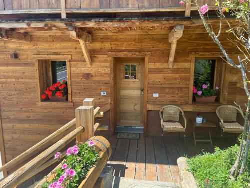 a wooden cabin with a porch with chairs and flowers at CASA VITTORIA in Gignod