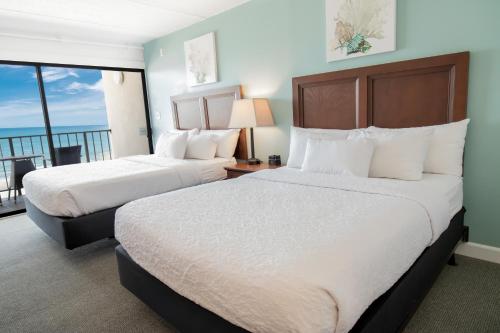 two beds in a hotel room with a balcony at Oceanfront Litchfield Inn in Pawleys Island