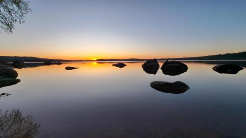 a sunset on a lake with rocks in the water at Safaritent 'Skogen' in Hagfors