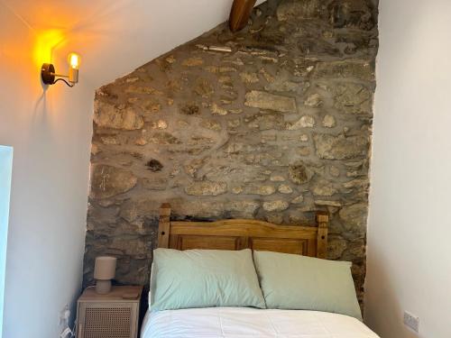 Bett in einem Zimmer mit einer Steinmauer in der Unterkunft Cosy modern miners cottage in Llanllechid