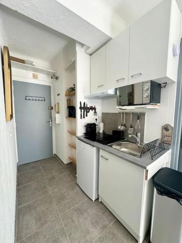 - une cuisine avec des placards blancs, un évier et une porte dans l'établissement Studio cosy à 5 min de la mer, à Villeneuve-Loubet