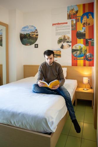 a man sitting on a bed reading a book at Hotel Trieste Mare in Lignano Sabbiadoro