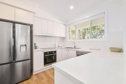 Una cocina con gabinetes blancos y un refrigerador de acero inoxidable. en A Coastal Hideaway, en Port Macquarie