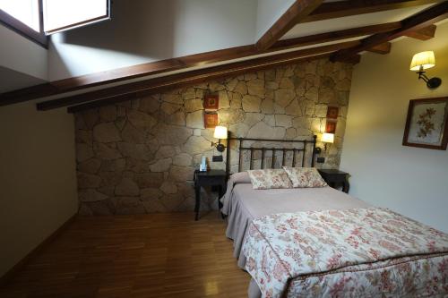a bedroom with a bed and a stone wall at Hotel Rural y Restaurante, Rinconcito de Gredos in Cuevas del Valle