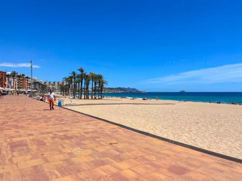 a person walking on a beach with palm trees and the ocean at Sol y Mar Villajoyosa in Villajoyosa