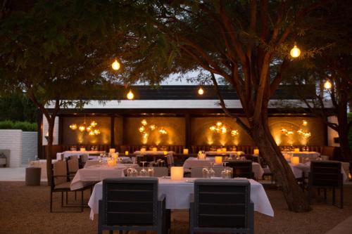 a restaurant with white tables and chairs under a tree at L'Horizon Resort & Spa, Hermann Bungalows in Palm Springs