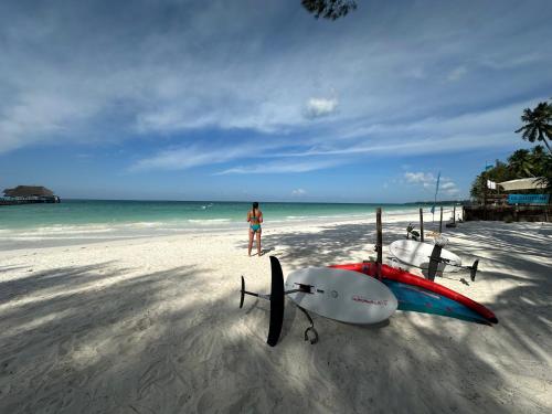 a person standing on a beach with a surfboard and a boat at Kiwengwa Bungalow Boutique Resort in Kiwengwa